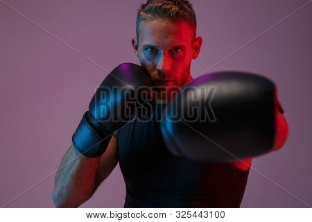 Image of a handsome strong young sports man boxer posing isolated over neon lights in gloves make boxing exercises.