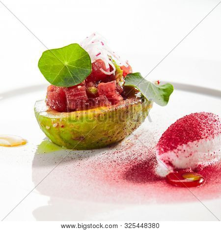 Tuna tartar made from raw fish served in avocado with lime ice cream on white restaurant plate isolated. Exquisite serving yellowfin sashimi tatar in alligator pear with gourmet dessert closeup