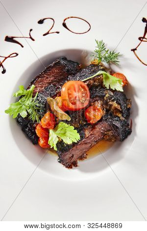 Exquisite serving white restaurent plate of grilled prime beef with tomatoes, spices and herbs topview. Restaurant main course with Well-done delicious veal meat, gourmet grillsteak isolated