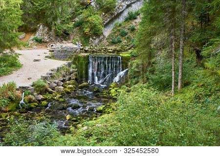Waterfall At Source Du Doubs Mouthe Franche Comté France With Green Plants On A Sunny Day