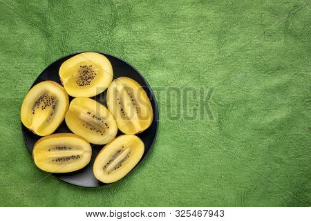 cut gold kiwifruit berries on black plate against green textured paper with a copy space