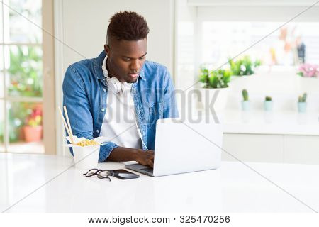 Handsome young african business man eating delivery asian food and working using computer concentrated