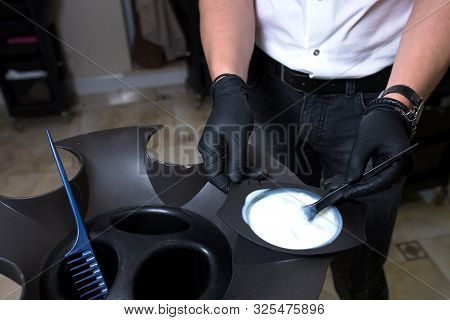 Male Stylist In Gloves Preparing Color Cream For Dying Hairin  A Container, A Mask For Treatment Pro