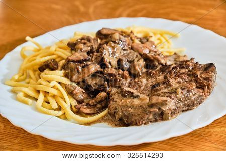 Tasty Beef Meat With Bolete Mushroon Sauce And Spatzle On White Plate On Wooden Table