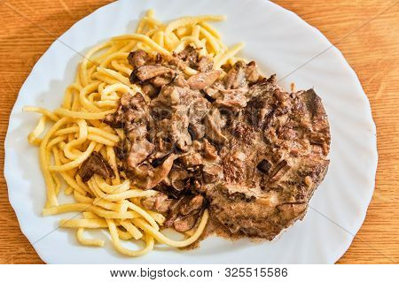 Tasty Beef Meat With Bolete Mushroon Sauce And Spatzle On White Plate On Wooden Table
