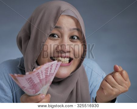 Portrait Of Indonesian Muslim Woman Holding Rupiah Money, Smiling Laughing Winning Gesture