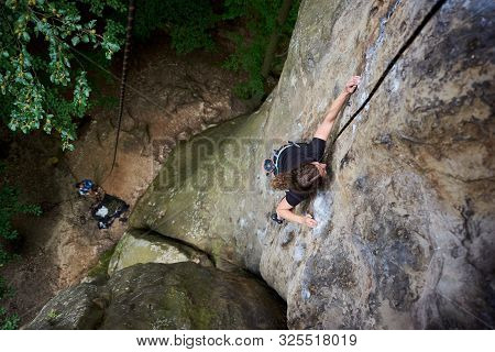 Young Female Rock Climber Climbing On Cliff With Safety Harness And Rope. Woman Overcoming Difficult