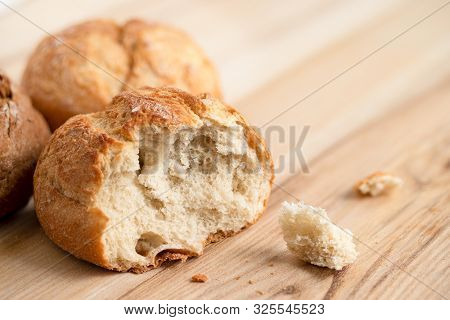 Broken Round Rustic White Bread Roll Next To Two Round Bread Rolls On Light Wood.