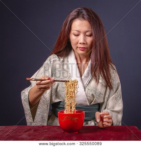 Beautiful Asian Woman With Long Hair In Kimono Eating Noodle With Wooden Chopsticks. Front View, Clo