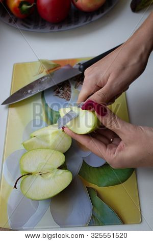 Women's Hands With A Bright Manicure Cut Green Apple With A Kitchen Knife