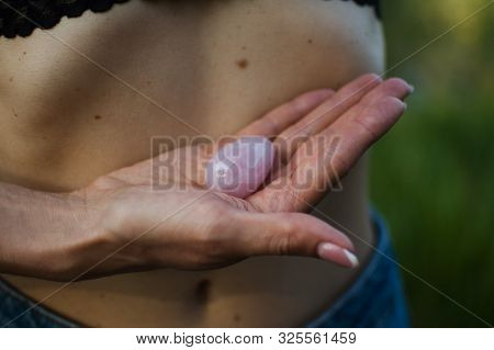 Adult Woman Is Holding Pink Quartz Yoni Egg For Vumfit, Imbuilding Or Meditation Outdoors Over Her N