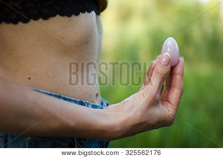 Side View Of Adult Woman Holding Pink Quartz Yoni Egg For Vumfit, Imbuilding Or Meditation Outdoors 