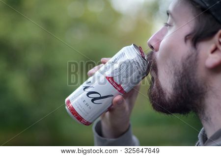 Sumy, Ukraine - August 10, 2019: Young Bearded Man Drinks Budweiser Bud Beer In Aluminium Can On Gre