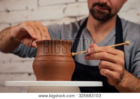 Handsome Young Potter Man In A Gray Sweater And A Black Apron Sculpts Clay Pot On A Potters Wheel In