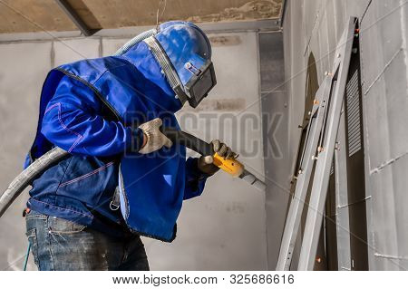 The Operator Of The Sandblasting Machine Is Ready To Go. The Worker Is Wearing A Safety Helmet And M