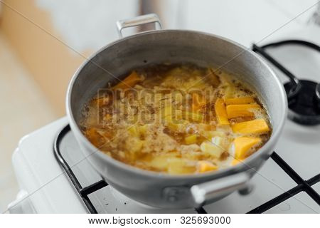 Pumpkin Soup Cooking In Sausepan In The Kitchen On The Stove. Autumn Traditional Food