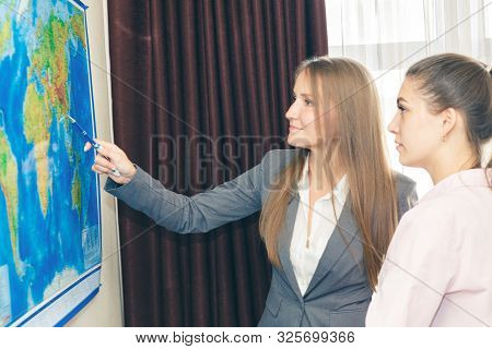 Two Business-like Young Women Plot A Route On A Geographical Map For The Delivery Of Cargo. Internat