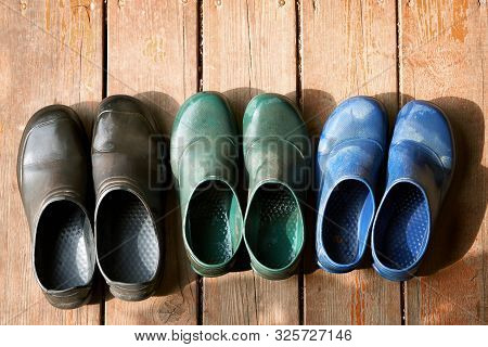 Three Pairs Of Old Family Rubber Boots On The Wooden Floor