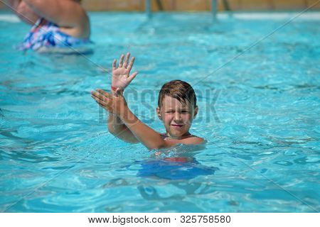 Smiling Caucasian Boy Having Fun In Swimming Pool At Resort. He Dancing Aqua Zumba And Claping Hands