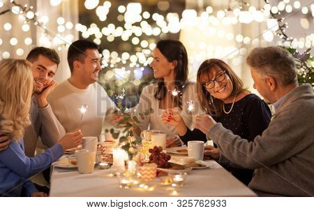 celebration, holidays and christmas concept - happy family with sparklers having fun at dinner party at home