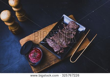 Beef Steak Cut Into Strips On A Cutting Board With Tomato Sauce Next To It And With Kitchen Utensils