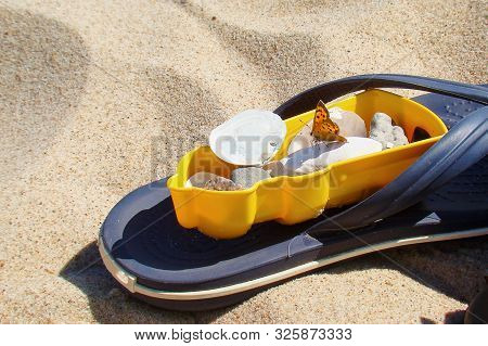 A Blue Flipflop Sandal Lies In The Fine Sand. On It Lies A Yellow Lighthouse Children Sand Mold, Fil