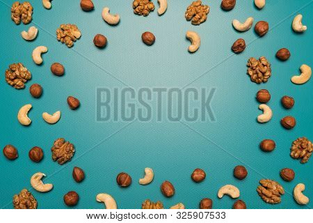Background Of Cashew Nuts, Walnuts, Hazelnuts With A Blank Space For Text. Scattered Nuts On A Blue 