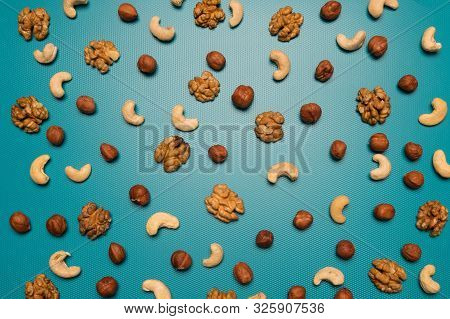 Background Of Cashews, Walnuts, Hazelnuts. Scattered Nuts On A Blue Background. Background From Diff