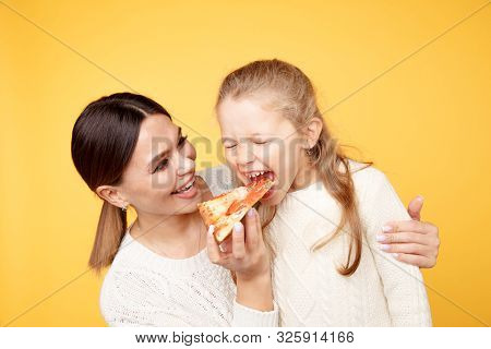 Mother And Daughter Eating Pizza Together And Having Fun Iolated Over The Yellow Studio.