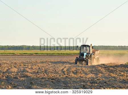 Plowed Field With A Working Tractor At Sunny Day In Belarusian Polesie.
