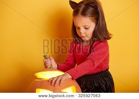 Close Up Portrait Of Cute Girl Playing With Her Halloween Pumpkin, Kid Wearing Sweater And Black Ski