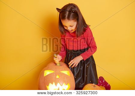 Close Up Portrait Of Cute Little Girl Wearing Cat Costume, Posing With Pumpkins, Looking Down On Her