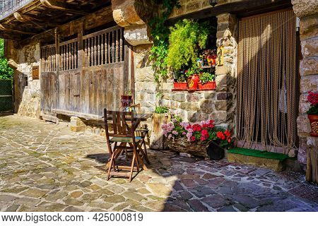 Facade Of Old Stone House With Wooden Table And Chair At The Door.