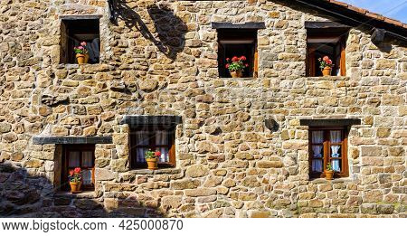 Facade Of An Old Stone House With Many Windows And Flower Pots.
