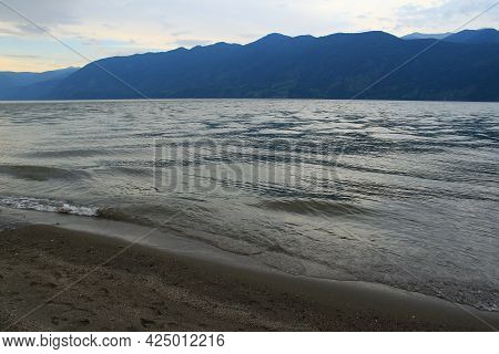 Sandy Shore On The Bartogai Reservoir, Light Waves On The Lake, A Mountain Range In The Distance, Su