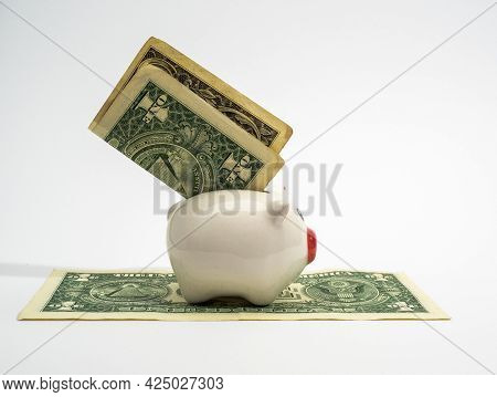 A Piggy Bank With A Dollar Stands On A Dollar, A White Background.