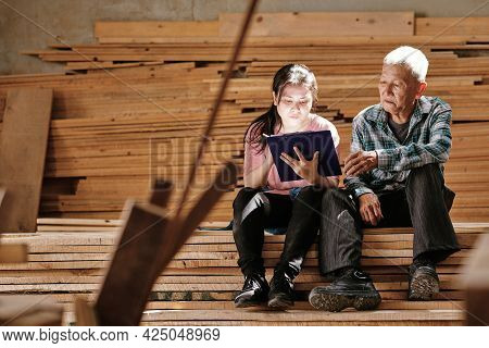 Ceative Young Woman Drawing Sketch On Clipboard To Show Grandfather Her Idea Of New Woodwork Project
