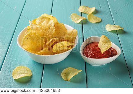 Delicious Potato Chips With Dill And Thick Tomato Ketchup In White Ceramic Bowls Over Blue Wooden Ta
