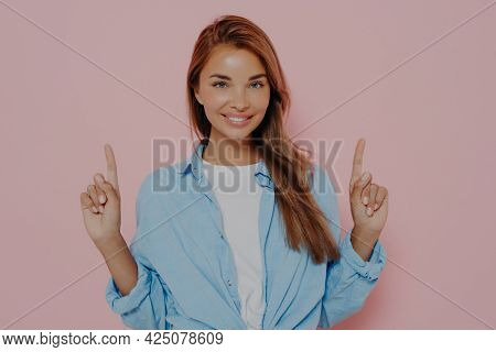 Happy Young Female Points Upwards With Index Fingers With Broadly Smile, Shows Awesome Item On Sale,