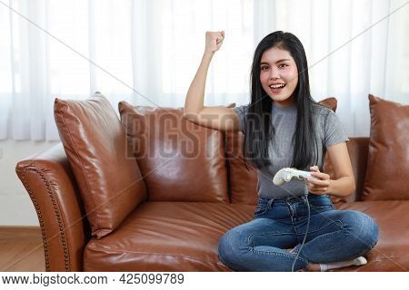 Vdo Game Console Station Concept. Active Asian Woman Sitting On Sofa, Holding Joystick And Playing E