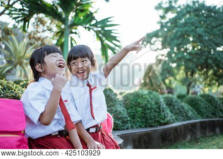 Two Asian Student In Uniform Pointing Away While Sitting Togehter