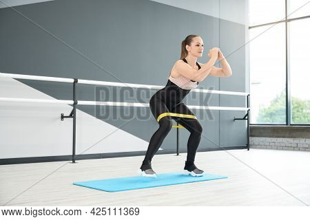 Side View Of Adult Woman In Tight Black Sportswear Using Fitness Band And Walking In Half Squat. Mus