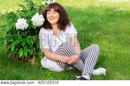 Portrait Of  Beautiful Woman Of Forty-five Years Old With Brown Hair, Sitting On Green Lawn In Sun A