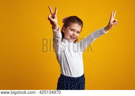 Girl Showing Peace Gesture With Both Raised Hands Against Yellow Background