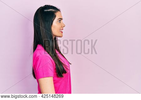 Young hispanic girl wearing casual pink t shirt looking to side, relax profile pose with natural face and confident smile. 