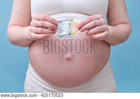 A Condom In The Hands Of A Pregnant Woman, A Studio Photo On A Blue Background