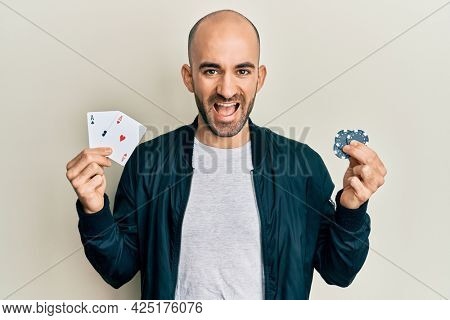 Young hispanic man playing poker holding casino cards and chips smiling and laughing hard out loud because funny crazy joke. 