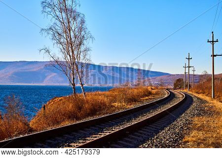 Circum Baikal Railway Running Along The Shore Of Lake Baikal On An Autumn Sunny Day With A Yellow La