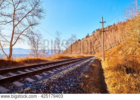 Circum Baikal Railway Running Along The Shore Of Lake Baikal On An Autumn Sunny Day With A Yellow La
