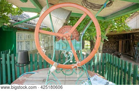 An Old Water Well With A Bucket In The Garden, A Metal Handle For Lifting Water From The Ground. Vil